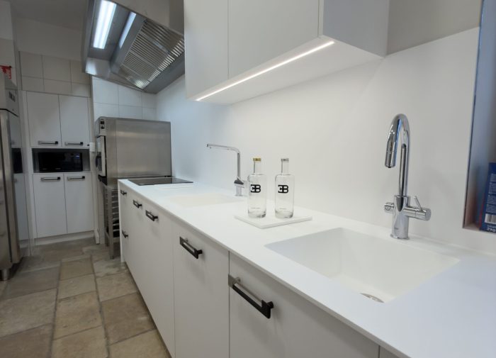 Plan de travail blanc avec éviers intégrés et robinetterie moderne pour une cuisine professionnelle au design minimaliste réalisée pour le projet cuisine Bugatti.