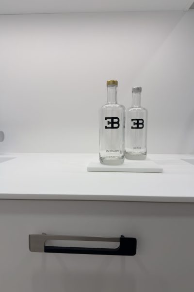 Gros plan sur des bouteilles en verre personnalisées avec le logo EB sur un plan de travail blanc épuré pour une cuisine haut de gamme au design minimaliste du projet cuisine Bugatti.