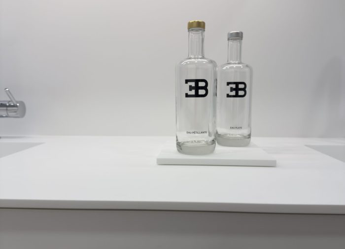 Gros plan sur des bouteilles en verre personnalisées avec le logo EB sur un plan de travail blanc épuré pour une cuisine haut de gamme au design minimaliste du projet cuisine Bugatti.