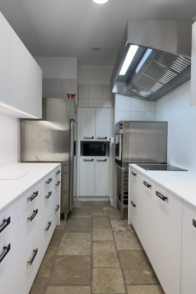 Vue d'ensemble d'une cuisine professionnelle au design minimaliste avec meubles blancs et équipements inox pour le projet cuisine Bugatti.