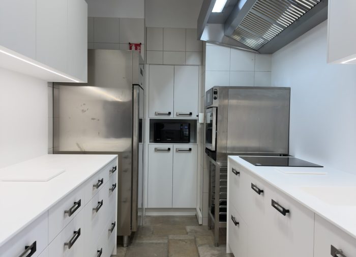 Vue d'ensemble d'une cuisine professionnelle au design minimaliste avec meubles blancs et équipements inox pour le projet cuisine Bugatti.