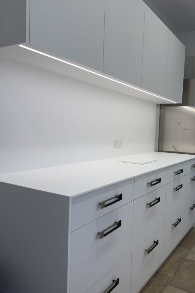 Vue en perspective de grands tiroirs blancs avec poignées profilées noires et éclairage LED intégré pour une cuisine haut de gamme au design minimaliste dans le cadre du projet cuisine Bugatti.