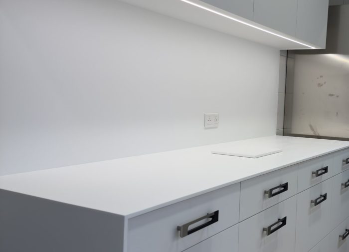 Vue en perspective de grands tiroirs blancs avec poignées profilées noires et éclairage LED intégré pour une cuisine haut de gamme au design minimaliste dans le cadre du projet cuisine Bugatti.