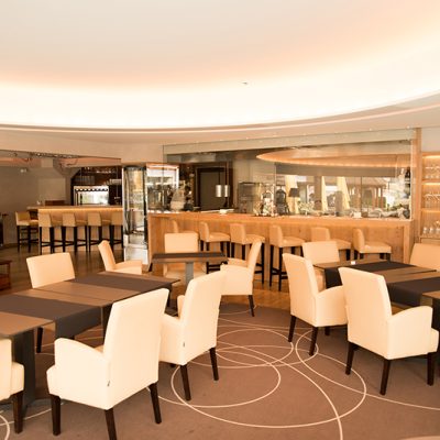 Salle à manger avec tables en bois foncé et chaises blanches disposées harmonieusement, avec un comptoir de bar en arrière-plan — un agencement contrasté et raffiné signé Arche du Bois, alliant convivialité et élégance dans un espace de restauration chaleureux.