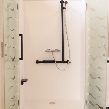 Cabine de douche Danaé by L'Arche du Bois vue de face, portes ouvertes sur un intérieur blanc épuré, équipé d'une barre de maintien et d'une barre d'appui verticale en I.