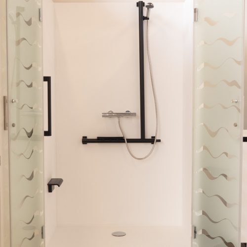 Cabine de douche Danaé by L'Arche du Bois vue de face, portes ouvertes sur un intérieur blanc épuré, équipé d'une barre de maintien et d'une barre d'appui verticale en I.