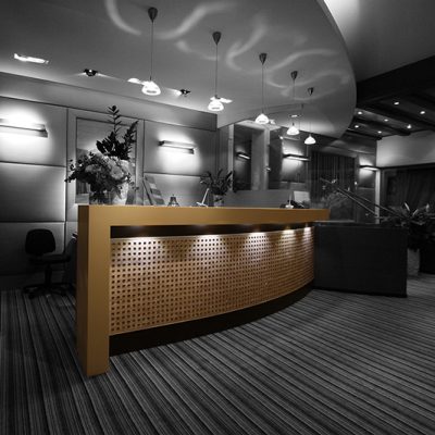 Comptoir arrondi de couleur marron, avec un éclairage intégré au-dessus et en dessous, conçu par Arche du Bois pour créer une atmosphère chaleureuse et accueillante dans l’espace d’accueil.