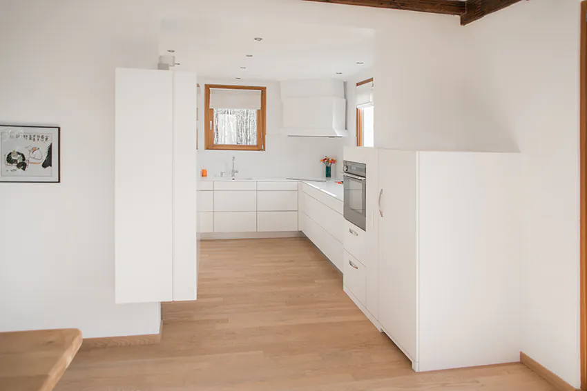 Cuisine au design blanc épuré avec meubles et murs blancs, contrastée par un sol en parquet bois naturel — un agencement sobre et élégant réalisé par Arche du Bois.