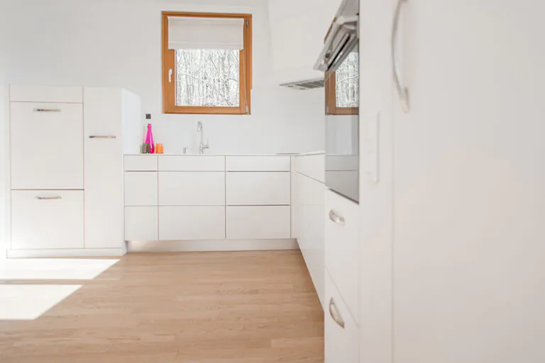 Vue d’une Cuisine sur mesure en Alsace avec agencement en L, comprenant des armoires sur le mur de droite et en face, ainsi qu’une fenêtre intégrée dans le mur du fond pour un éclairage naturel